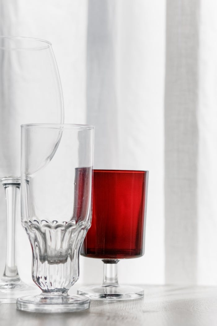 Close-up of diverse glassware featuring a striking red glass on a clean white surface.